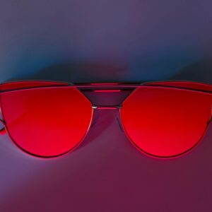 Stylish sunglasses with red lenses on a colorful gradient backdrop. Perfect for fashion and accessory themes.
