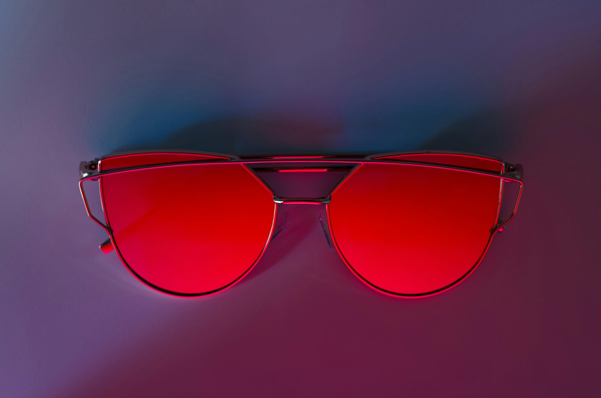 Stylish sunglasses with red lenses on a colorful gradient backdrop. Perfect for fashion and accessory themes.