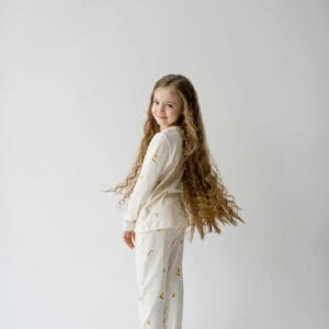 A young girl with long hair wearing pajamas poses against a white background, smiling over her shoulder.