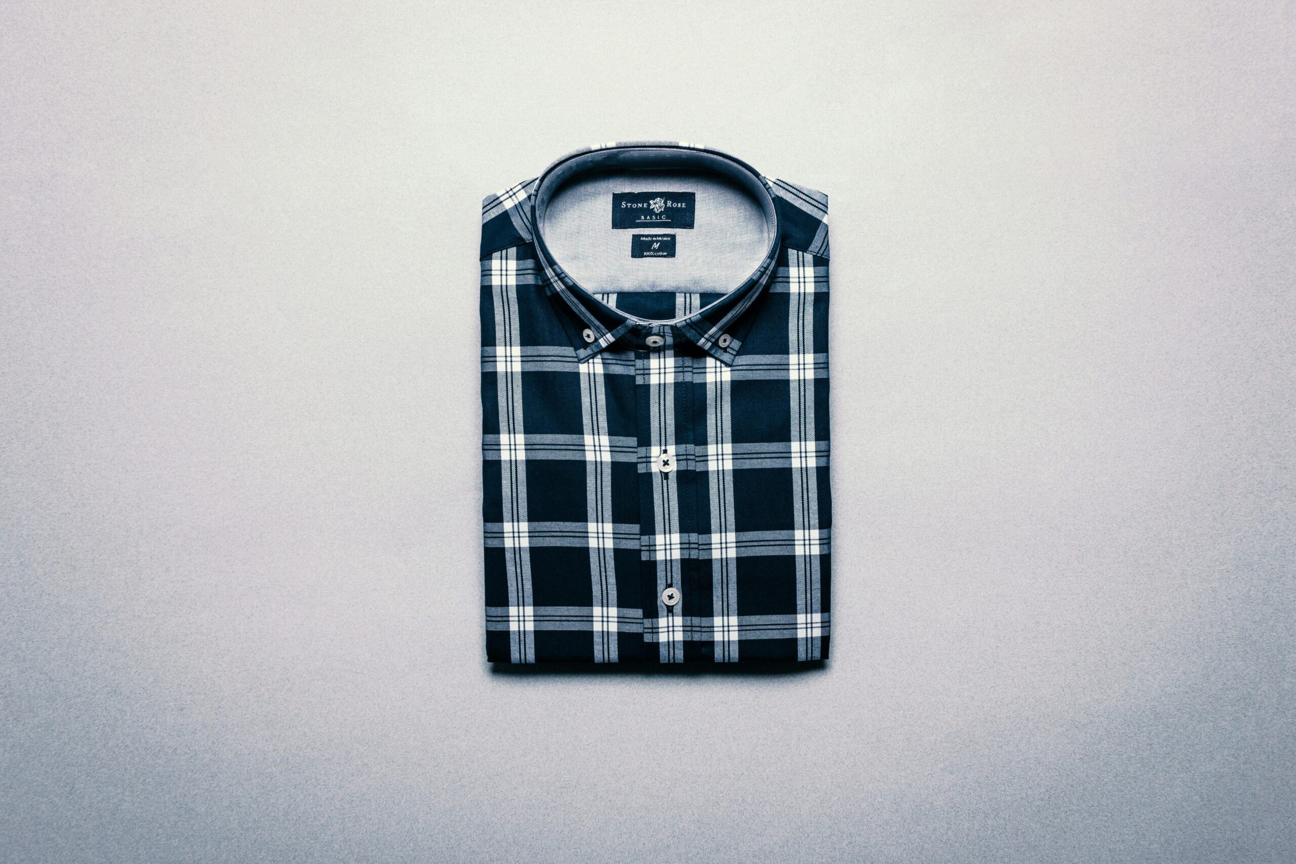 Neatly folded plaid shirt displayed on a flat gray surface, top view.