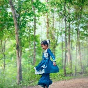 A young girl in traditional dress dances joyfully in a sunlit forest clearing.