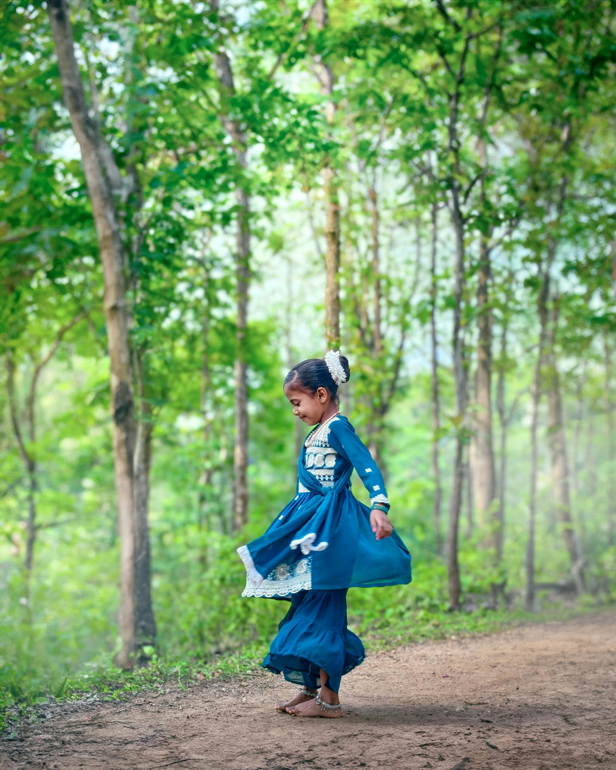A young girl in traditional dress dances joyfully in a sunlit forest clearing.