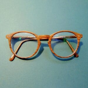 Close-up of fashionable wooden frame eyeglasses on a solid blue background.